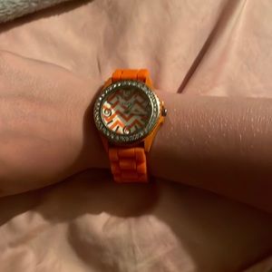 This is a neon orange wrist watch. There are rhinestones around the clock.